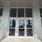 Glass double doors of a modern building reflecting surrounding landscape, showcasing Oratso Corp's door solutions.