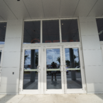 Double glass doors of a modern commercial building, showcasing Oratso Corporation's door solutions in South Florida, with reflections of the surrounding environment visible.