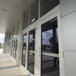Modern glass doors with sleek silver frames at a commercial building entrance, showcasing Oratso Corporation's door solutions for residential and commercial needs.