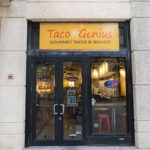 Taco Genius restaurant entrance showcasing gourmet tacos and nachos, featuring a bright orange sign above glass doors, located in a mall setting.