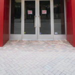 Double glass doors with exit signs, framed by red walls, at Sunset Place Mall, showcasing Oratso Corp's door installation.