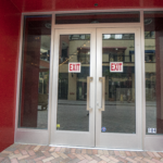 Double glass doors with "EXIT" signs, part of the Sunset Place Mall project by Oratso Corp, showcasing modern design and accessibility features.