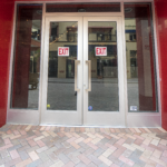 Glass double doors with exit signs, featuring a brick walkway, part of the Sunset Place Mall project by Oratso Corp, highlighting their door installations.