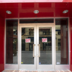 Glass double doors with red frame and exit signs, showcasing Oratso Corp's door installation at Sunset Place Mall.