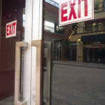 Exit doors with prominent "EXIT" signs, reflecting the entrance of a commercial space, part of the Sunset Place Mall project by Oratso Corporation.