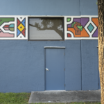 Colorful mural on blue wall featuring geometric patterns and a door, representing cultural art centers by Oratso Corp.