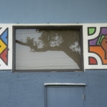 Window with tree reflection, vibrant mural artwork on blue wall, highlighting cultural art center themes.