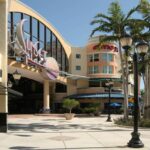 Sunset Place Mall entrance featuring modern architecture, large glass windows, and palm trees, showcasing Oratso Corporation's door and window installations.