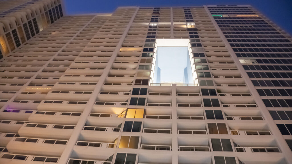 High-rise apartment building with modern architectural design, featuring a central void and illuminated balconies, showcasing Oratso Corporation's luxury apartment offerings in Miami.