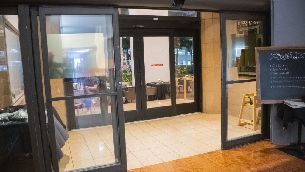 Entrance of a modern apartment building featuring glass automatic doors, showcasing interior seating and decor, emphasizing Oratso Corporation's stylish apartment offerings.