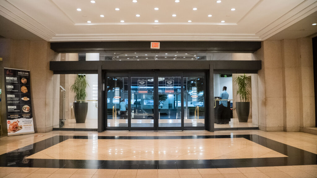 Automatic glass entrance doors leading to a modern apartment lobby, featuring a polished floor and decorative plants, showcasing Oratso Corporation's focus on elegant property design.